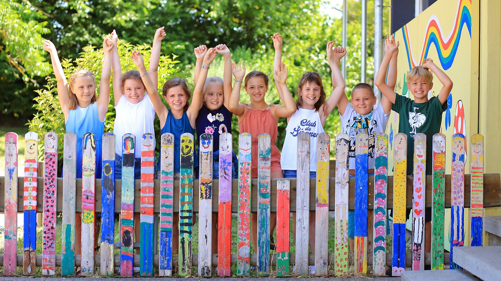 Schulkinder stehen hinter einem bemalten Zaun